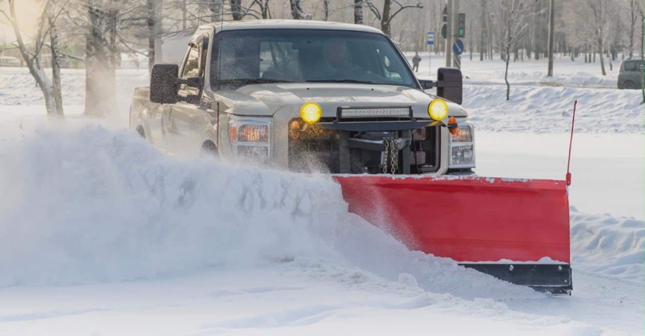 Pickup truck with a snow plow clearing a snow-covered street